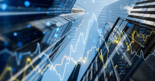 Upward view of city skyscrapers with overlaid stock market graphs and digital data elements.