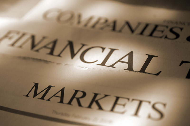 A sepia toned, close up image of a loosely stacked pile of sections of a generic financial broadsheet newspaper showing the sections headed ‘Companies’, ‘Financial’, and ‘Markets’. Shot with shallow depth of field with focus on the centre right of the image.
