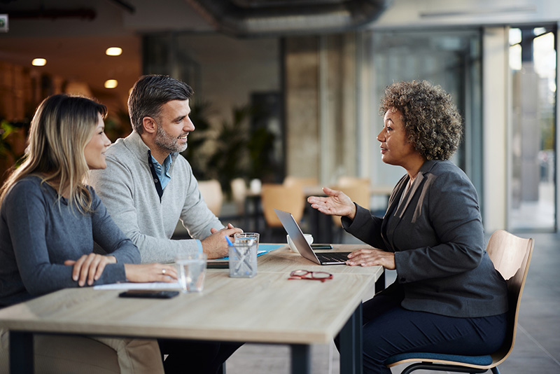 A couple sits at a take with a financial advisor, reviewing their investment portfolio.