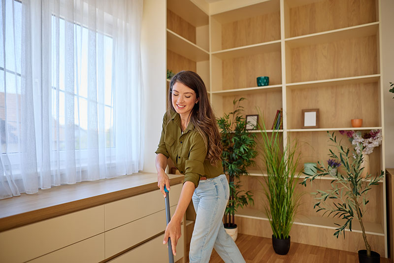 Young woman mopping her wood floors in a sunlit room